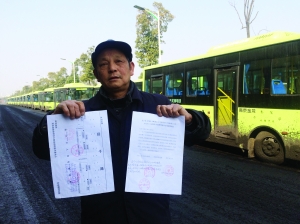 劉明手持多個部門的審批文件，身后就是閑置在路邊的電動公交車